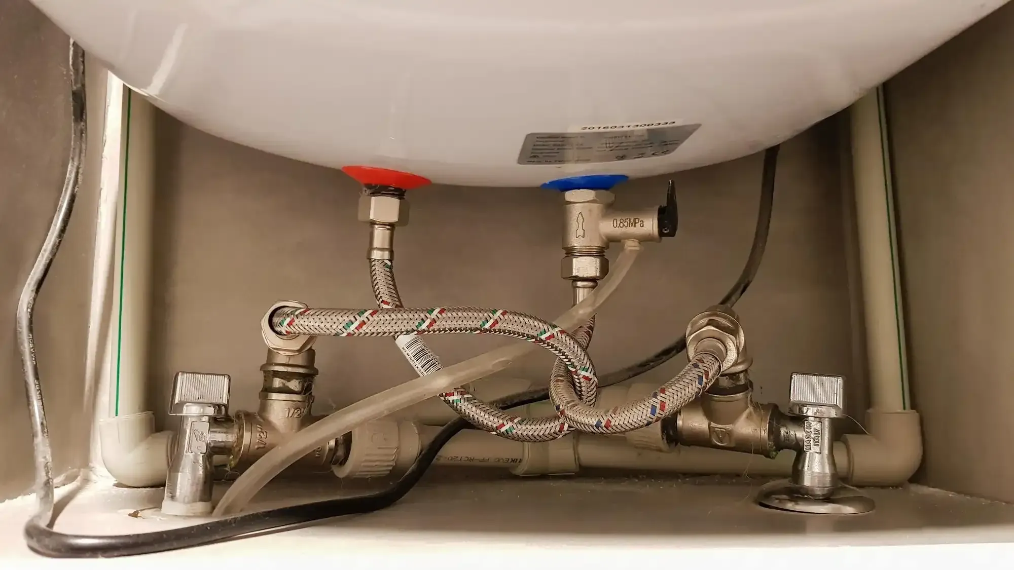 Braided supply hoses and shut-off valves connected beneath a wall-mounted tank water heater.